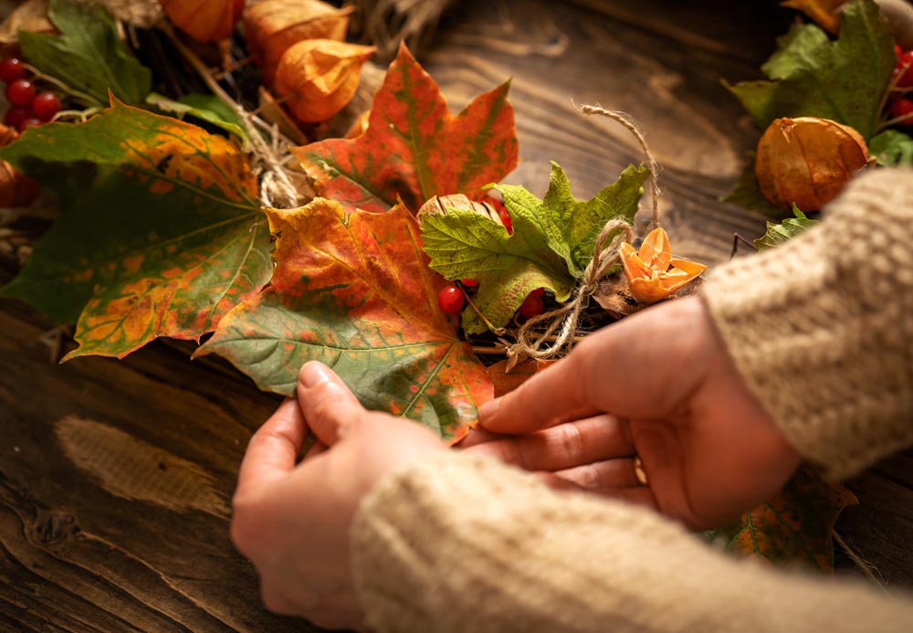 close up image of hands making a wreath out of fall leaves