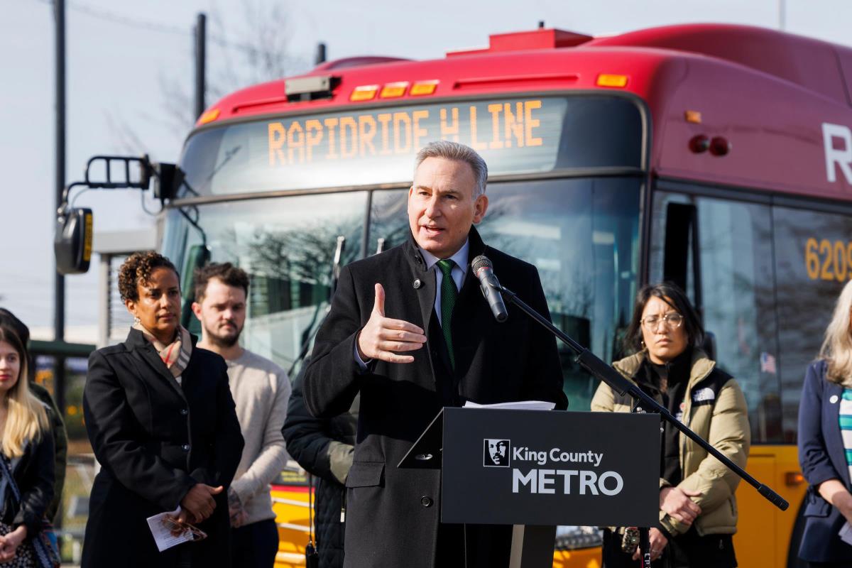 Dow Constantine speaks at a press conference with a Metro bus in the background.