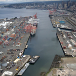 Aerial photo of the East Waterway, looking north. Shipping cranes line the waterway on both sides with downtown Seattle in the distance.