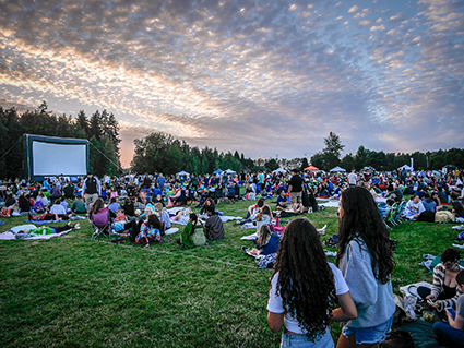 Movies at Marymoor in Redmond: audience gathering on the grass as the sun sets, young women in the foreground.