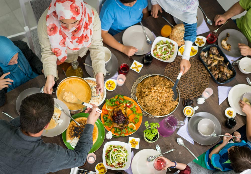 Green Ramadan header - overhead image of a dinner table with multiple dishes and people dining