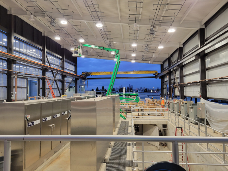 A view inside of the treatment station under construction. A green lift is being used to place equipment. Panels of equipment are in the foreground and the far wall is not constructed yet. 