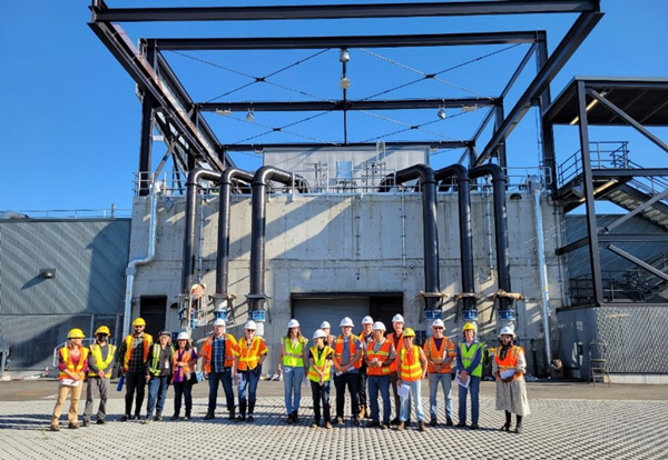 group of people in orange construction vests standing in front of a large industrial building
