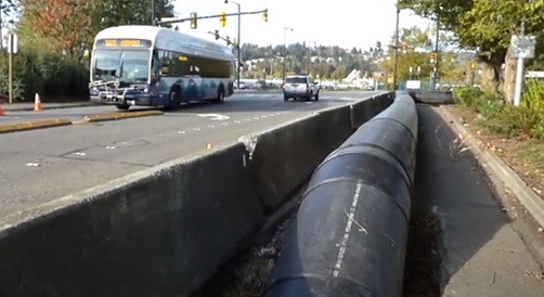 Image of a King County temporary pipe on a roadway. The pipe is on the far right-side of the roadway and protected by a concrete barrier.
