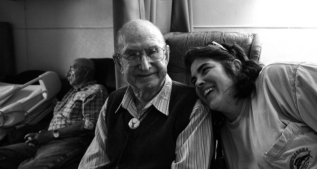 Elderly man poses with a laughing young woman in a nursing facility. 