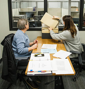 Two people sitting at a table and looking at folders in a box