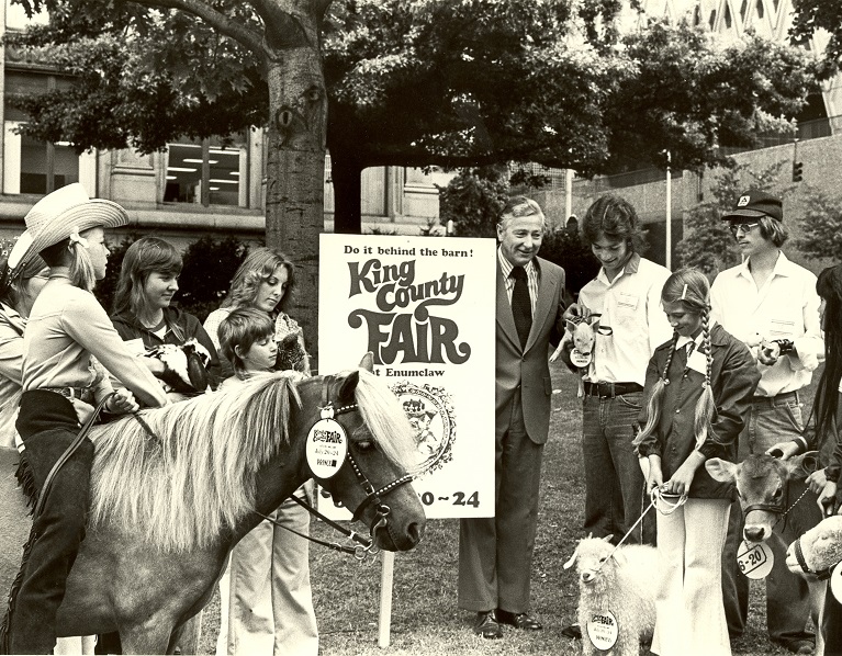 Children and farm animals standing next to a King County Fair sign