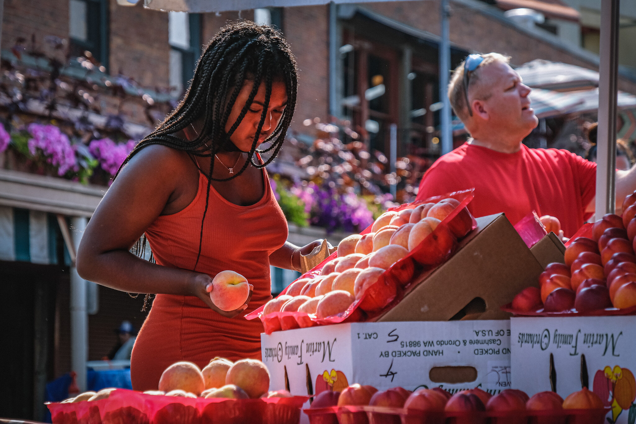 A young woman selecting peaches from a farmer's market stall.