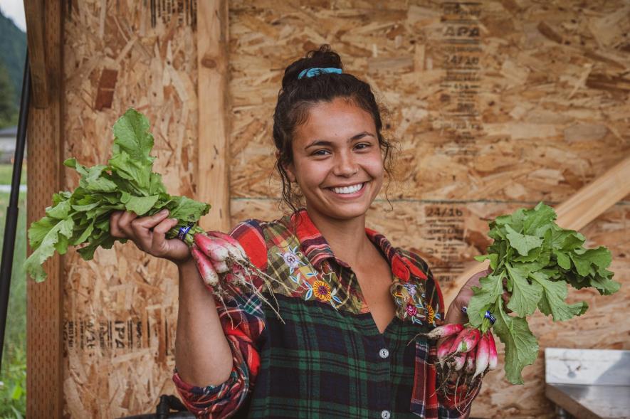 A young woman smiling, holding bushels of radishes.