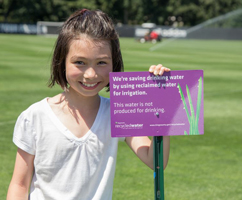 girl next to recycled water sign