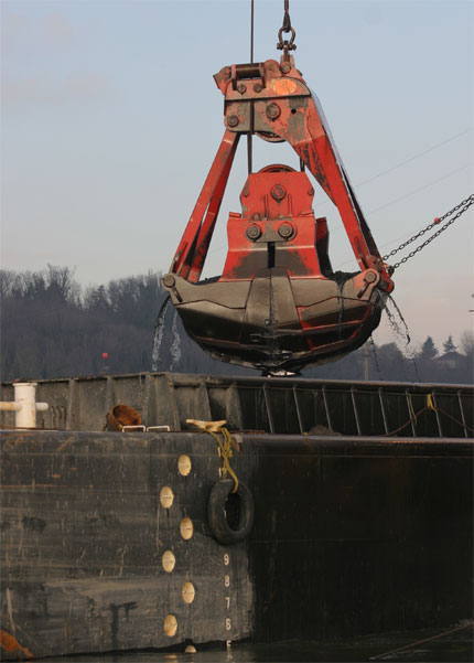 A large red shovel (dredge) with river sediment material above a barge