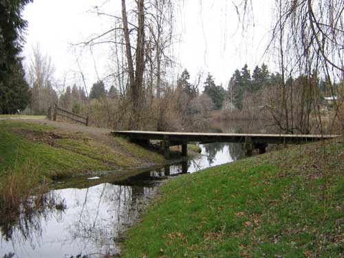 Photo of stream flowing out of a lake underneath a footbridge